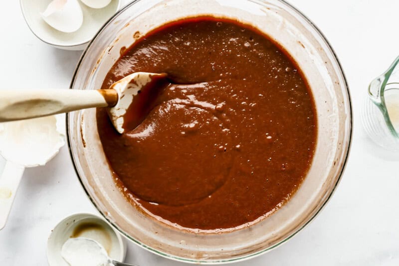 chocolate cake batter in a glass bowl with a rubber spatula.