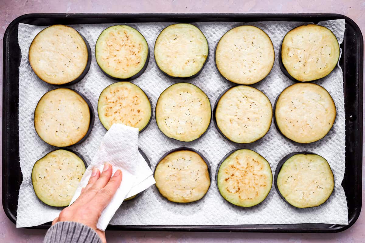 patting slices of eggplant dry on a baking sheet.