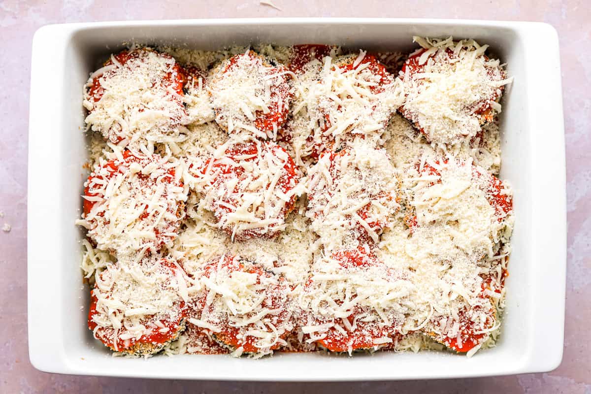 cheese sprinkled over eggplant parmesan in a baking pan.