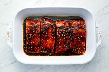 4 raw salmon fillets marinating in a white baking pan.