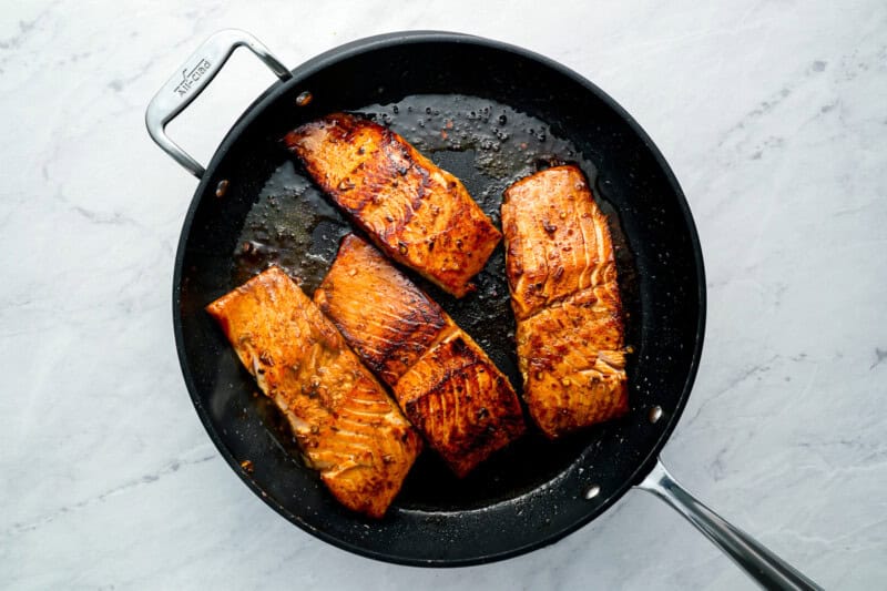 4 salmon fillets cooking in a frying pan.