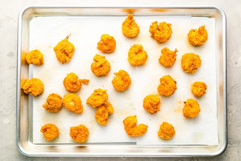 fried shrimp draining on a paper towel-lined baking sheet.