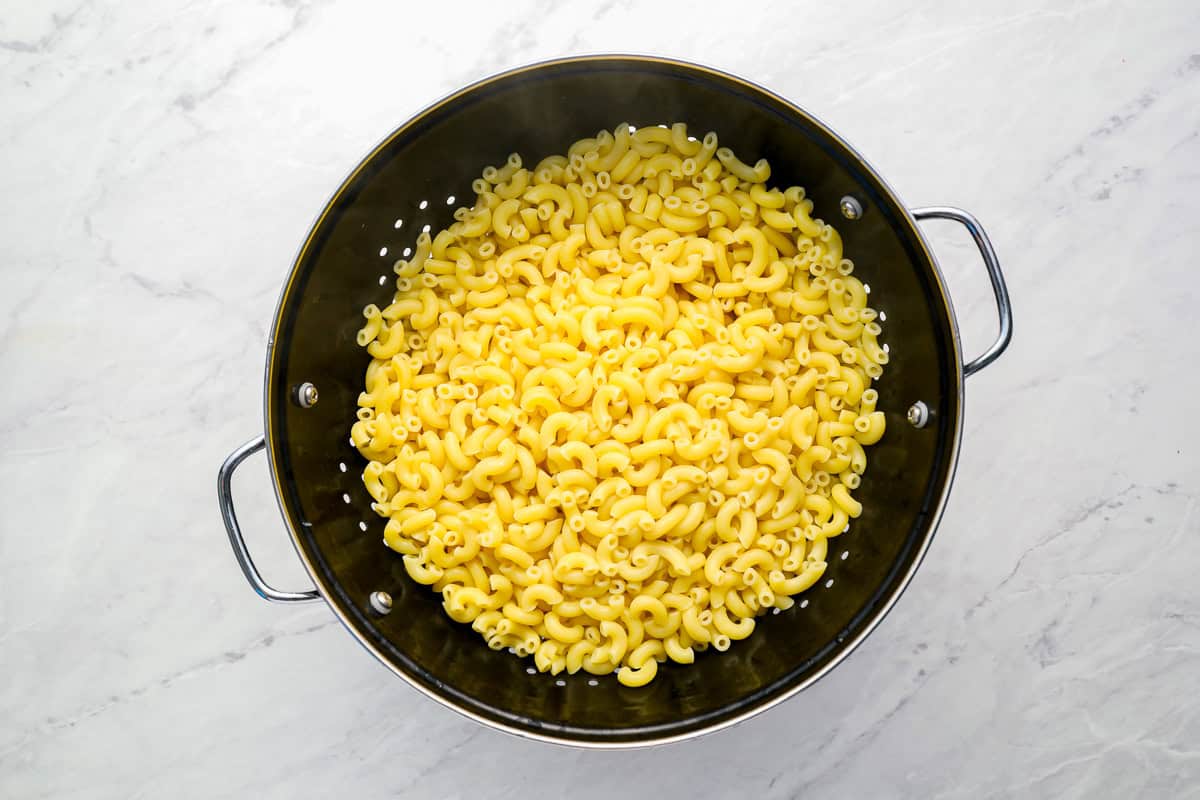 cooked macaroni noodles in a colander set over a pot.