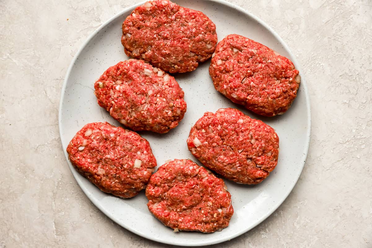 6 formed hamburger steak patties on a white plate.