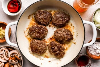 6 cooked hamburger steaks in a pan.