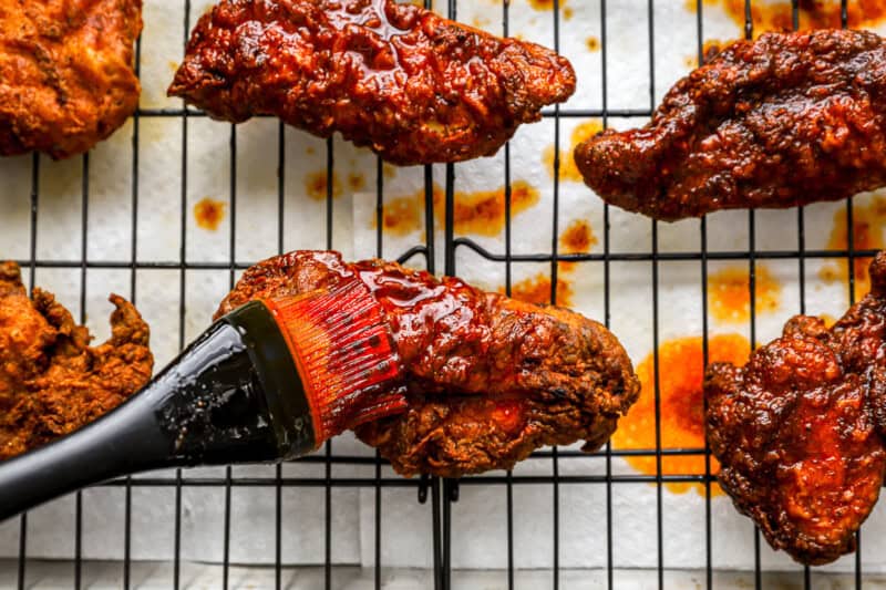 brushing sauce over nashville hot chicken with a pastry brush.