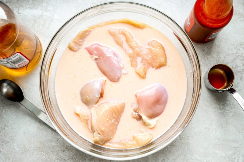 raw chicken marinating in buttermilk in a glass bowl.