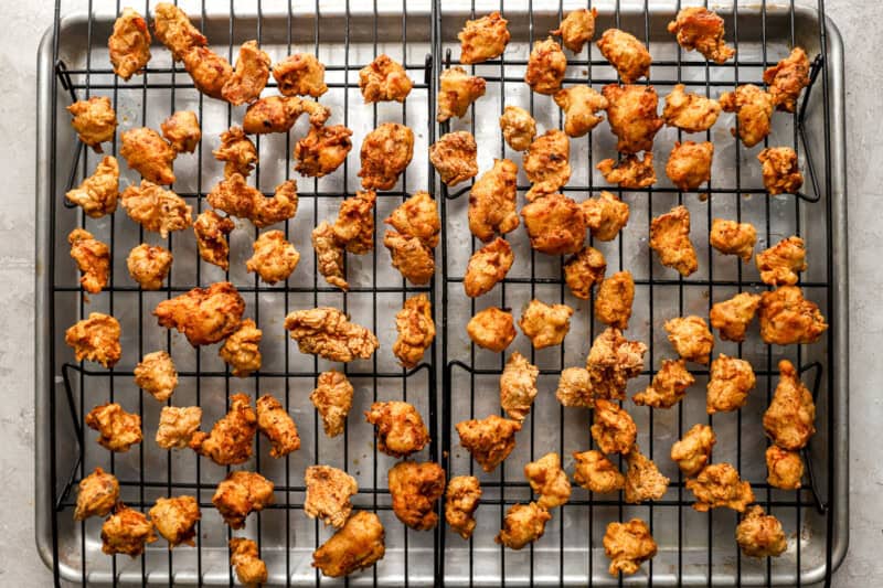 fried popcorn chicken pieces on a wire rack set in a baking sheet.