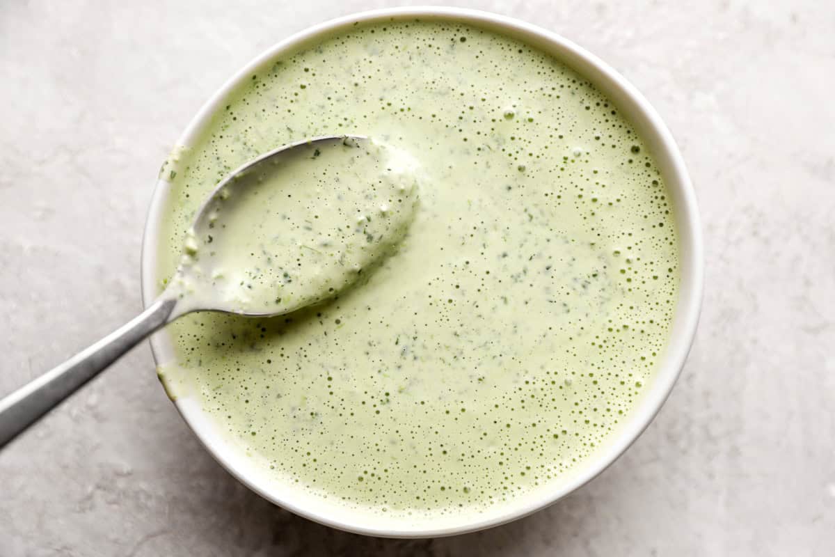 creamy cilantro dressing in a white bowl with a spoon.