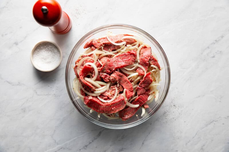 Mixing bowl filled with uncooked pieces of steak and onions.