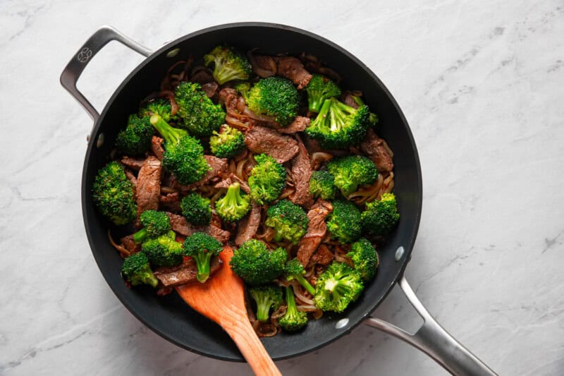 Broccoli florets and strips of steak sautéing in a skillet.