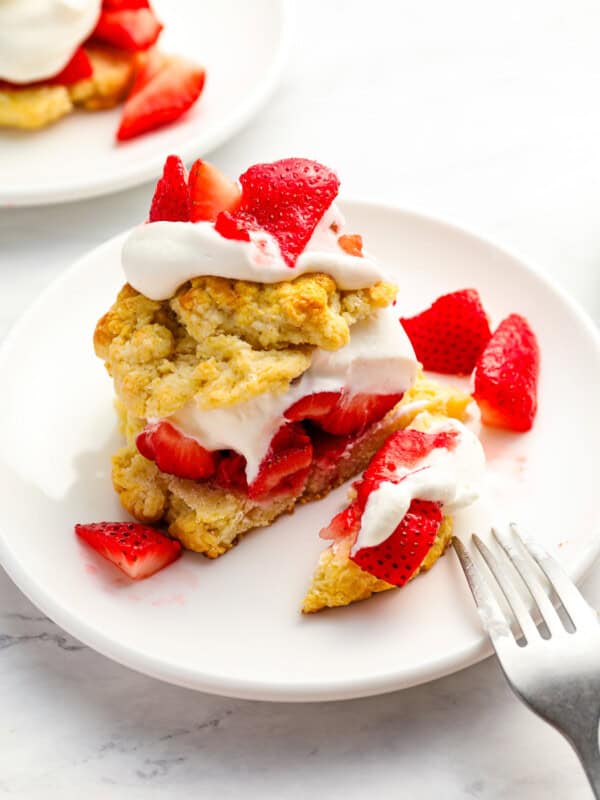 cut strawberry shortcake on a white plate with a fork.