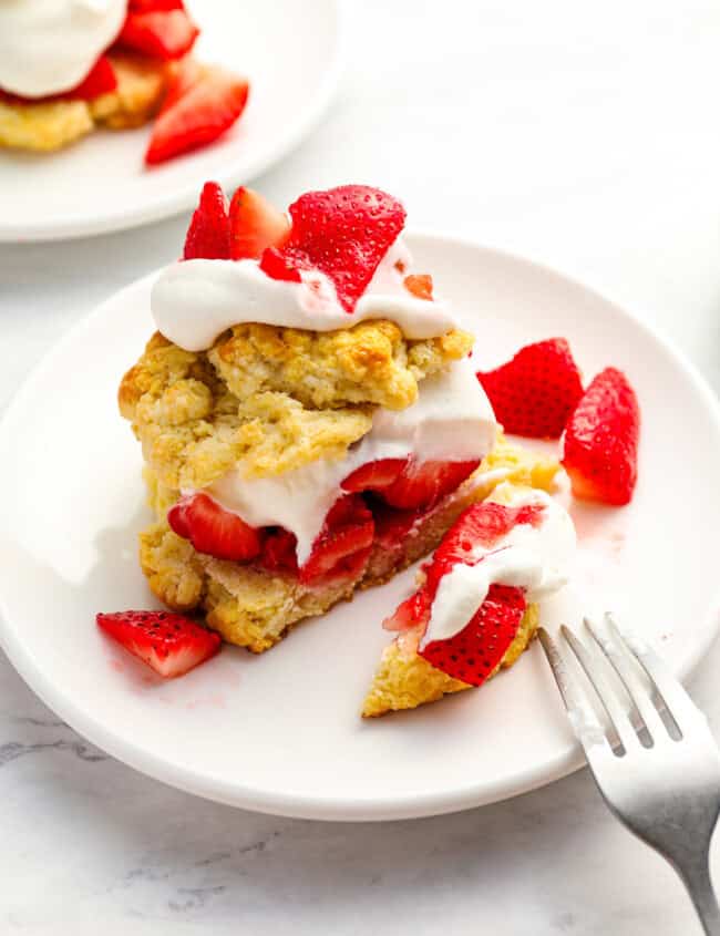 cut strawberry shortcake on a white plate with a fork.