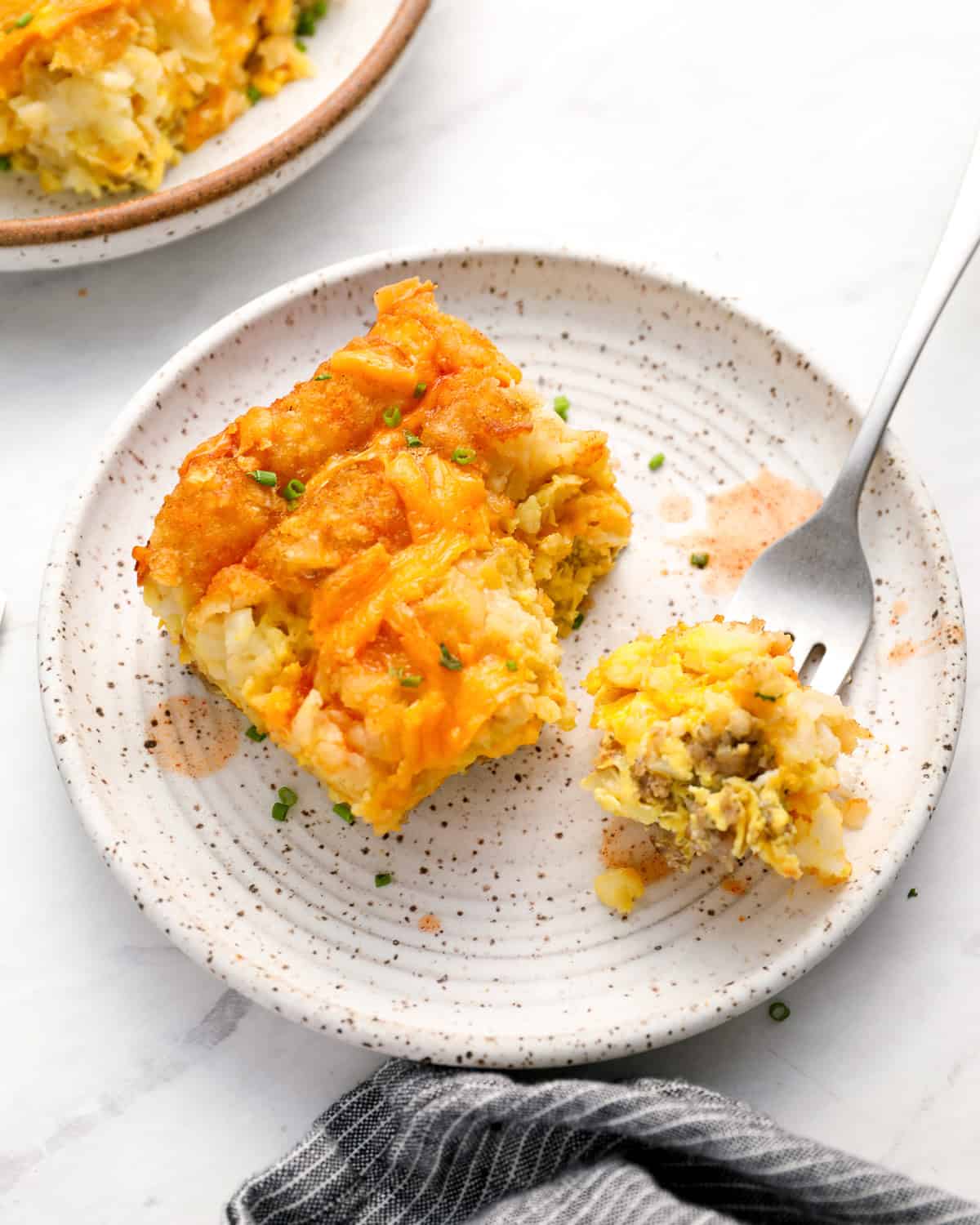 a partially eaten serving of tater tot breakfast casserole on a speckled plate with a fork.