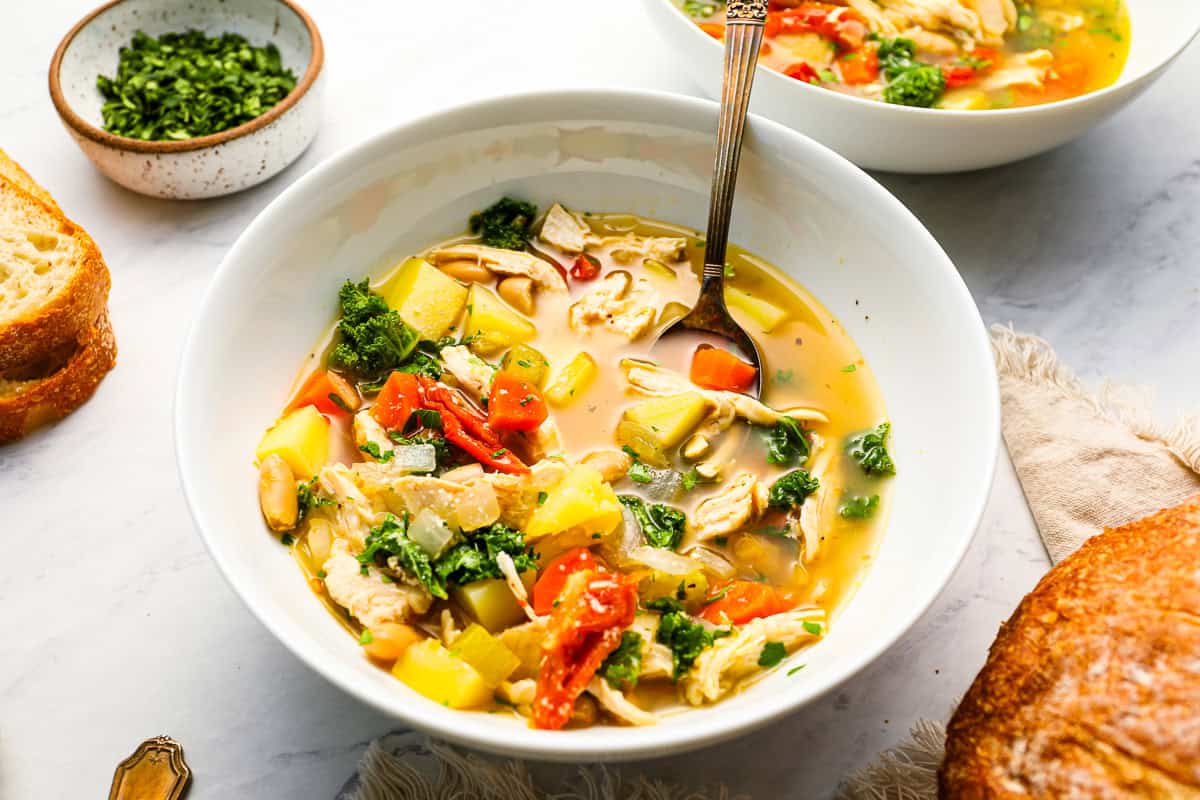 a serving of tuscan chicken soup in a white bowl with a spoon.