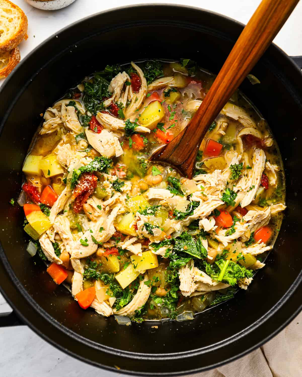 overhead view of tuscan chicken soup in a dutch oven with a wooden spoon.