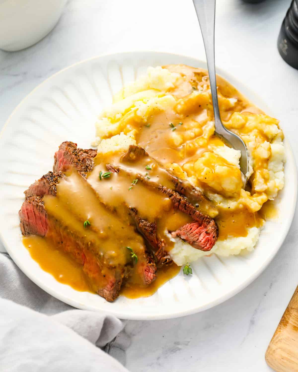 sliced steak and mashed potatoes topped with brown gravy on a white plate.