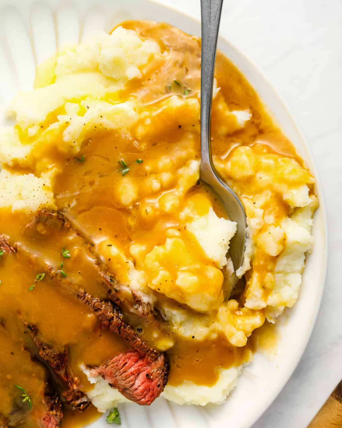 close up of brown gravy over mashed potatoes on a white plate.