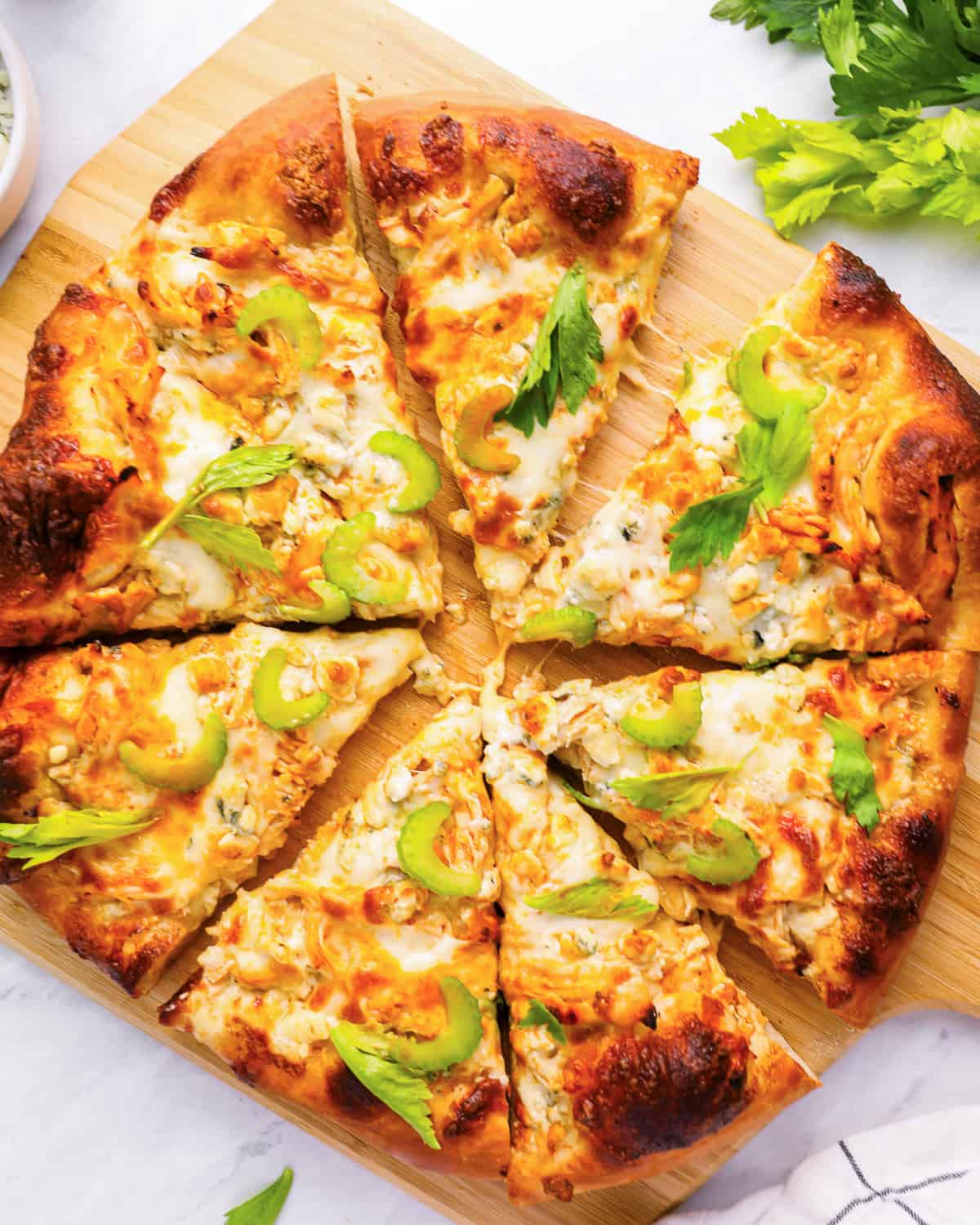 overhead view of a sliced buffalo chicken pizza on a wood pizza peel.