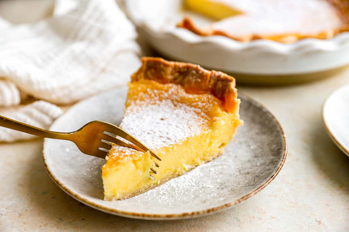 a fork cutting into a slice of chess pie on a speckled plate.