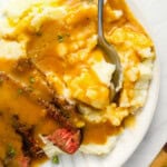 close up of brown gravy over mashed potatoes on a white plate.