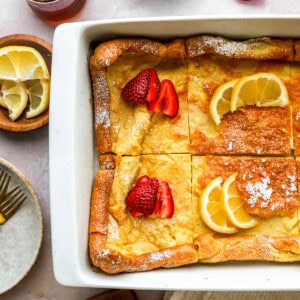 partial overhead view of a cut dutch baby in a rectangular baking pan with lemon slices and strawberries.