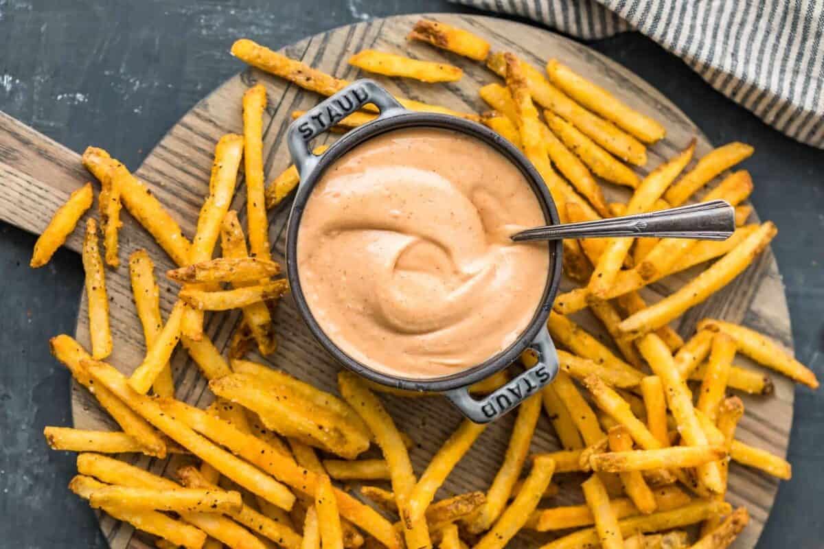 A bowl of French fries with fry sauce on a wooden cutting board.