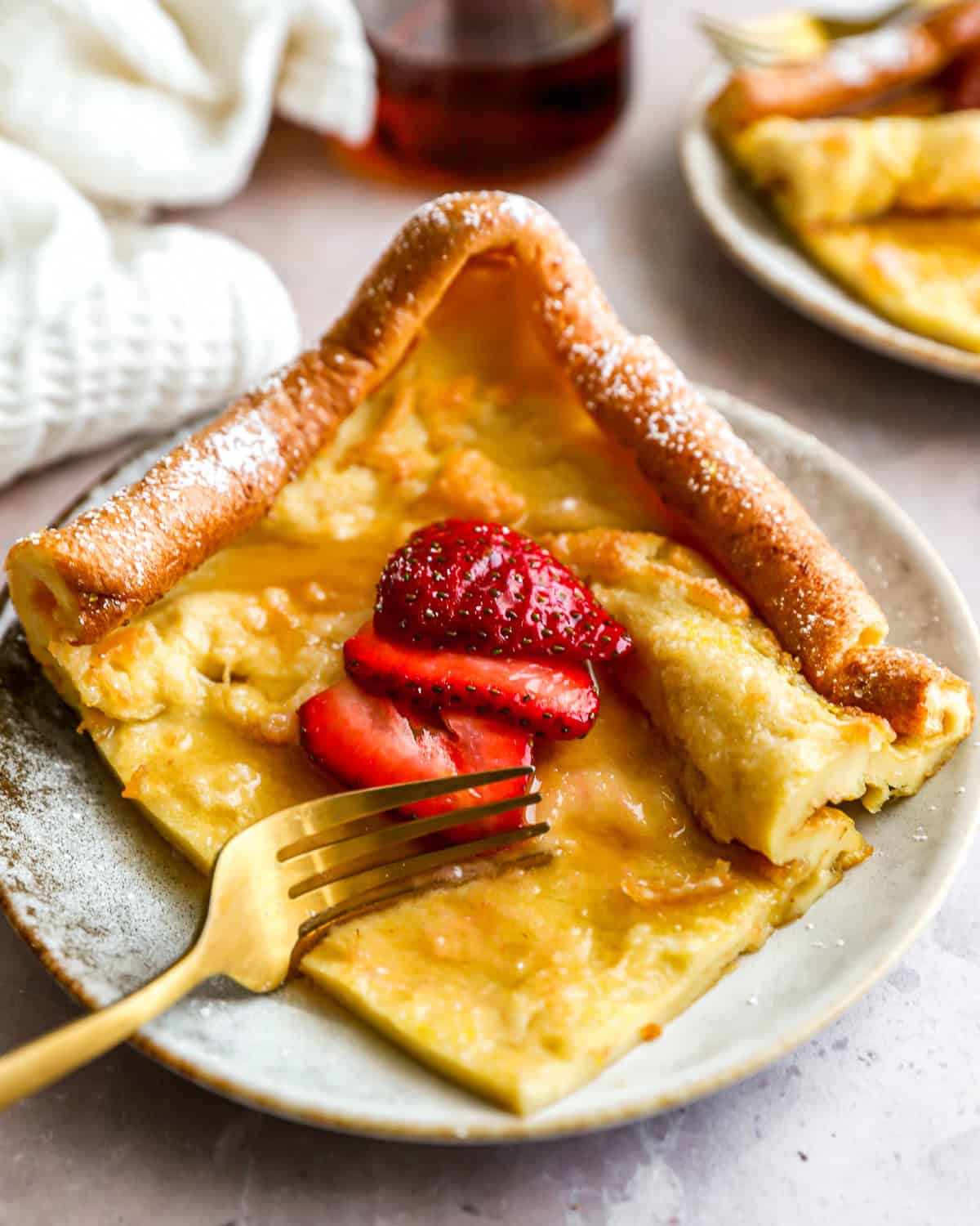 cutting a slice of German pancake on a plate with a fork.