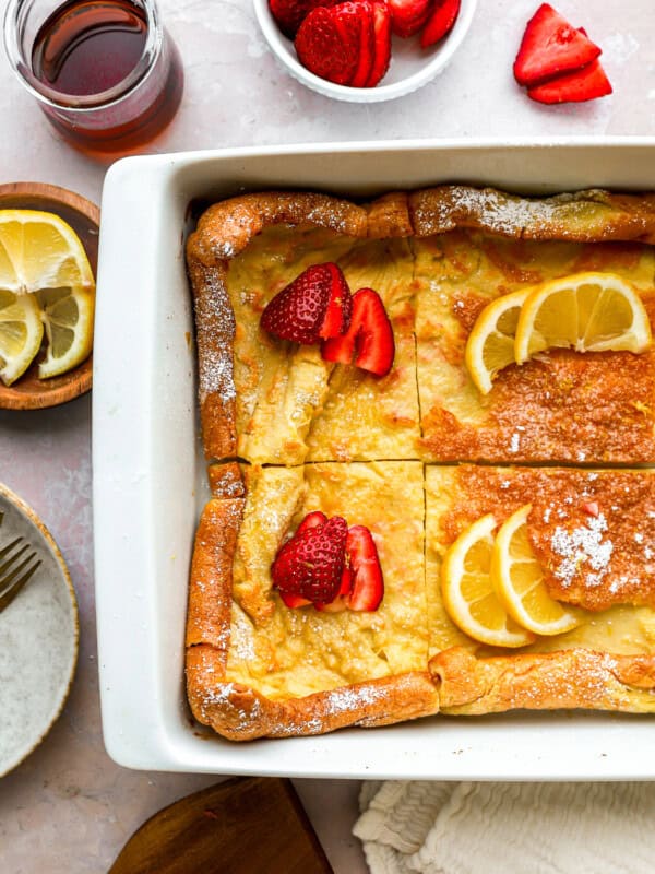 partial overhead view of a cut dutch baby in a rectangular baking pan with lemon slices and strawberries.