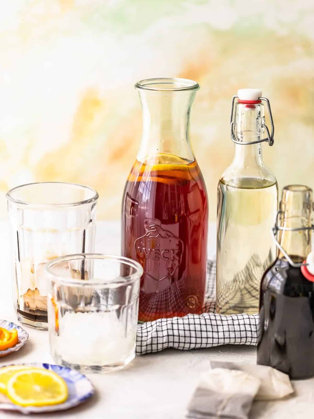 A pitcher of sweet tea, a jar of simple syrup, glasses of ice, and tea bags arranged on a countertop.
