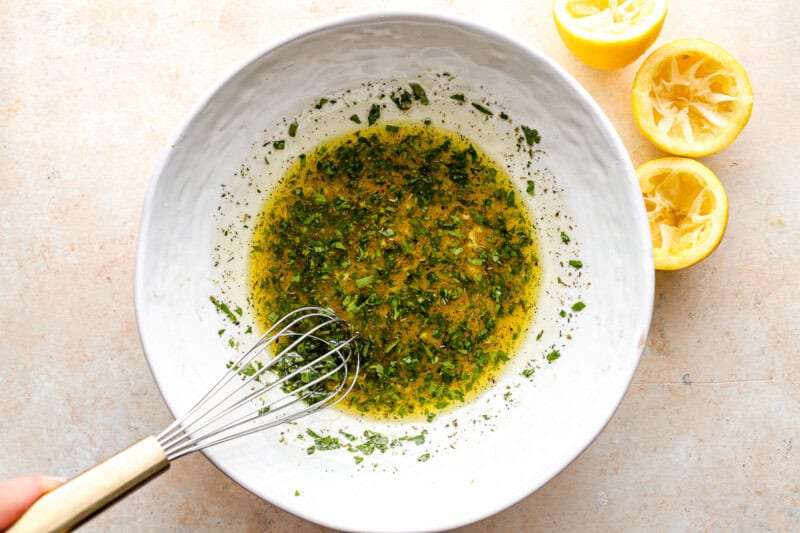 whisking herby dressing in a white bowl.