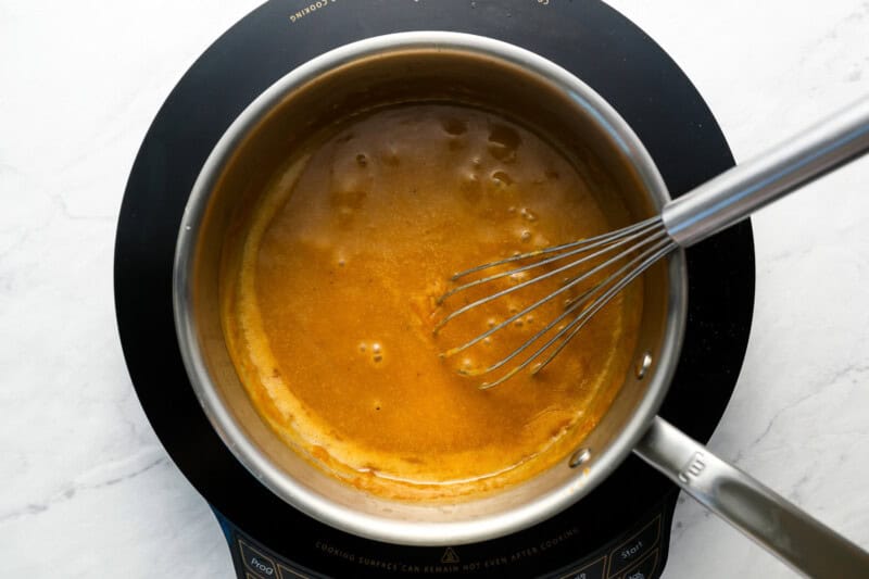 simmering brown gravy in a pot with a whisk.