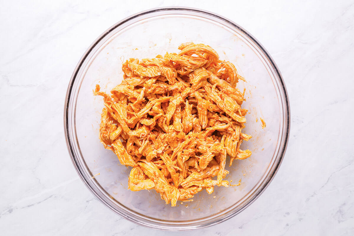 shredded chicken tossed in buffalo sauce in a glass bowl.