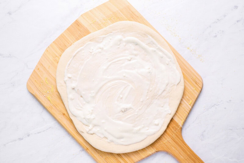 blue cheese dressing spread over pizza dough on a wood pizza peel.