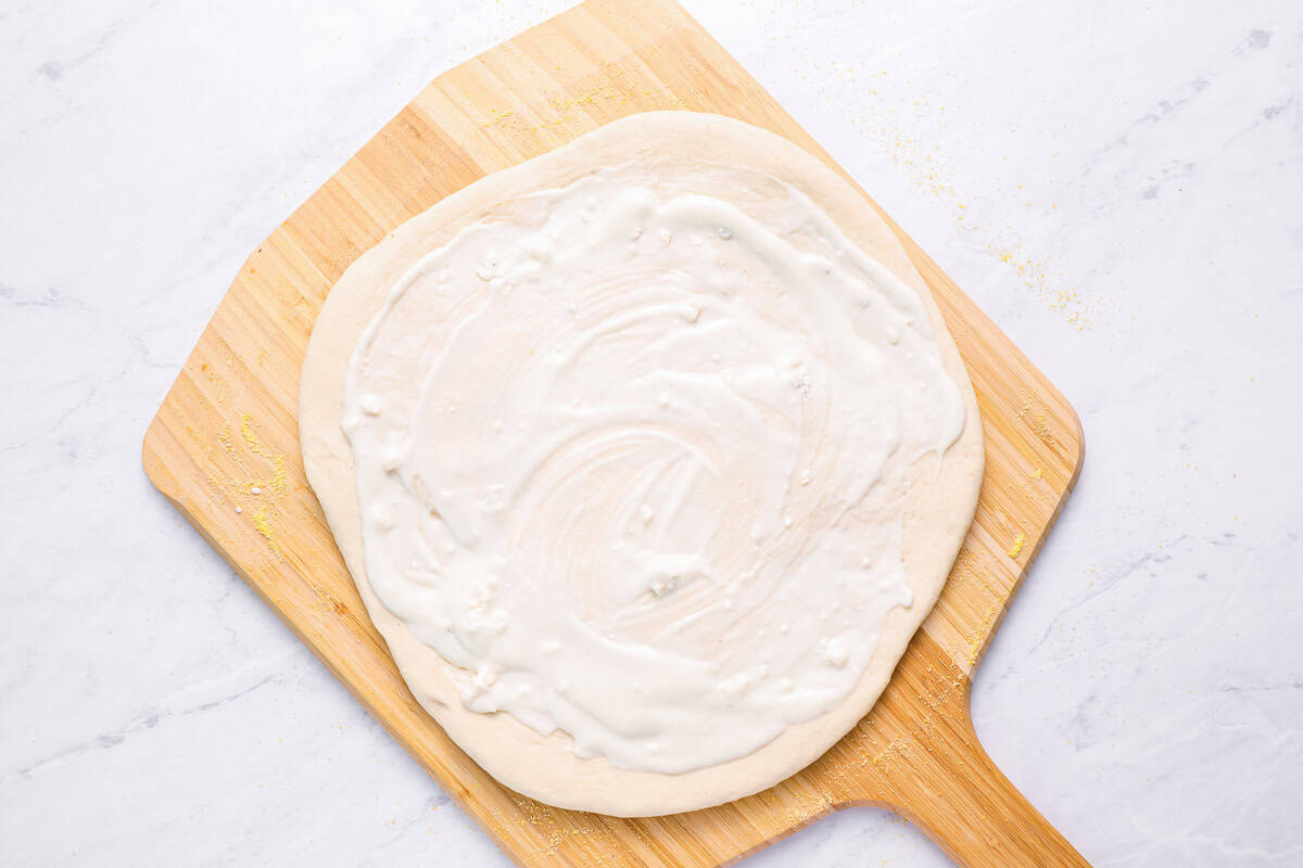 blue cheese dressing spread over pizza dough on a wood pizza peel.