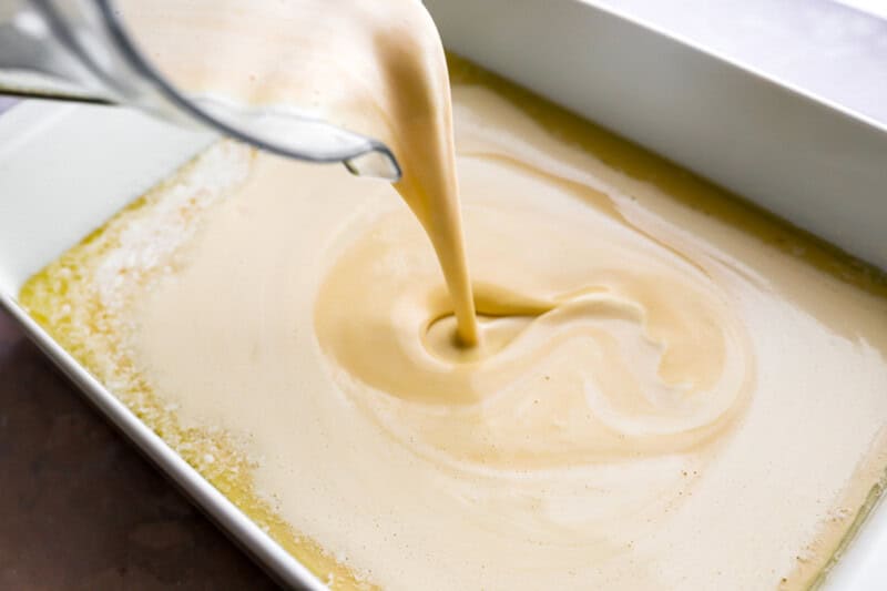 pouring pancake batter over melted butter in a baking pan.