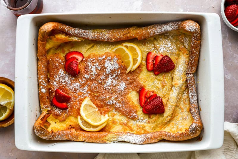 overhead view of a dutch baby in a rectangular baking pan with lemon slices and strawberries.