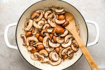 sauteed mushrooms in a dutch oven with a wooden spoon.