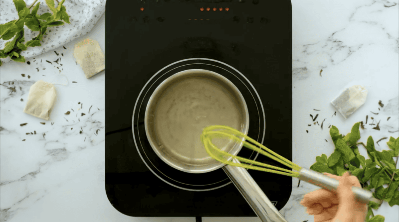 Whisking a liquid mixture together in a pot on an electric hot plate.