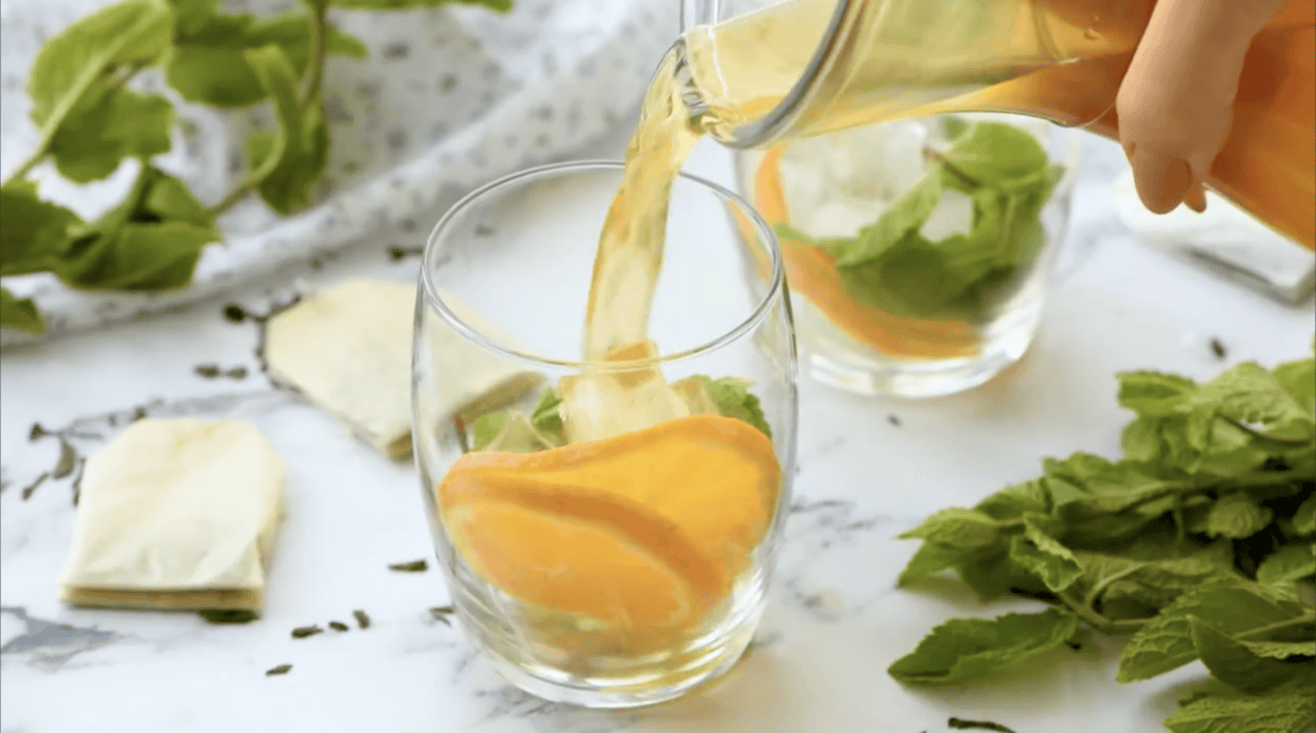 Pouring sweet tea into a glass filled with mint and oranges.