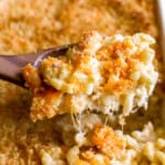 closeup view lifting a scoop of baked mac and cheese from a casserole dish with a wooden spoon.