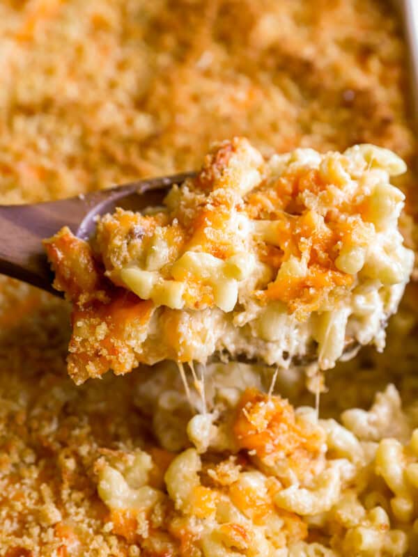 closeup view lifting a scoop of baked mac and cheese from a casserole dish with a wooden spoon.