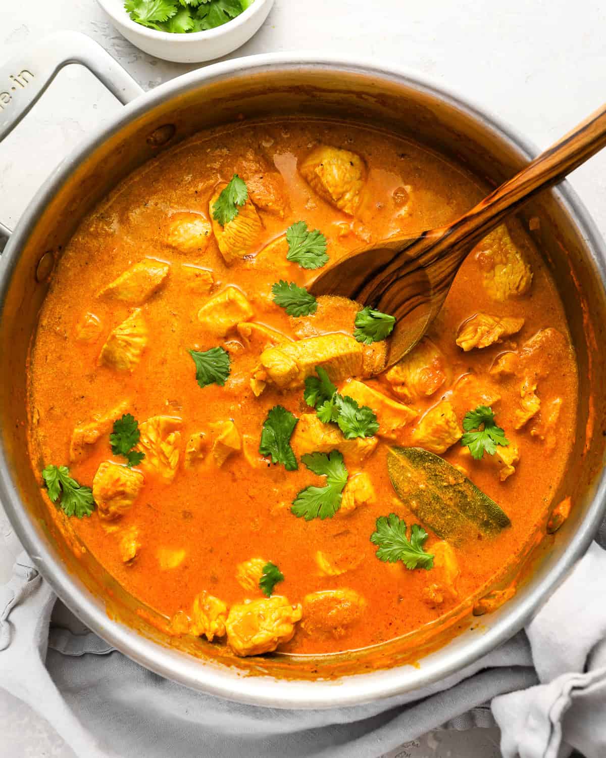 overhead view of chicken curry in a pan with a wooden spoon.