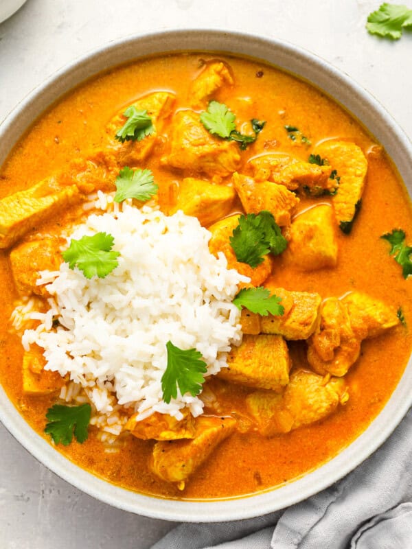 overhead view of a serving of chicken curry in a bowl with rice and cilantro.