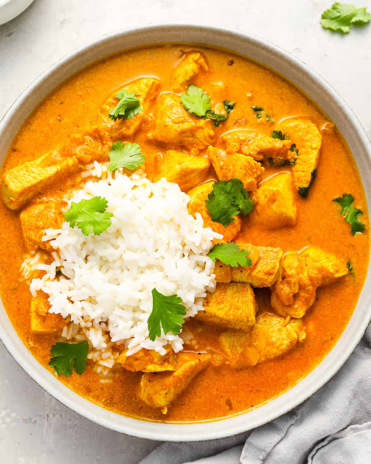 overhead view of a serving of chicken curry in a bowl with rice and cilantro.