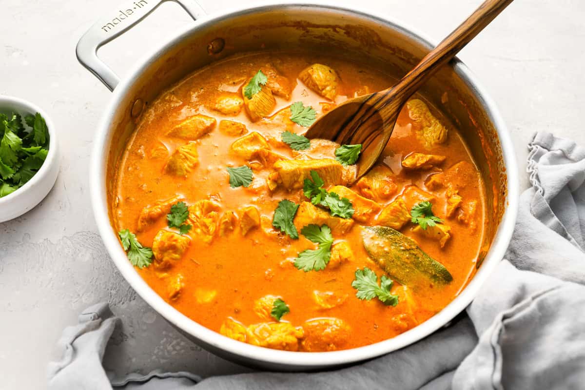 chicken curry in a pan with a wooden spoon.