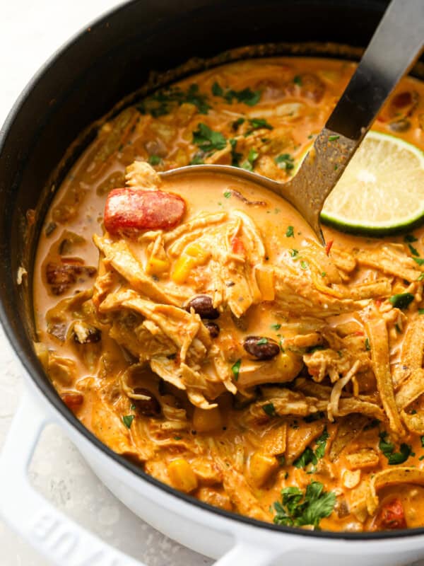 scooping chicken enchilada soup from a dutch oven with a ladle.