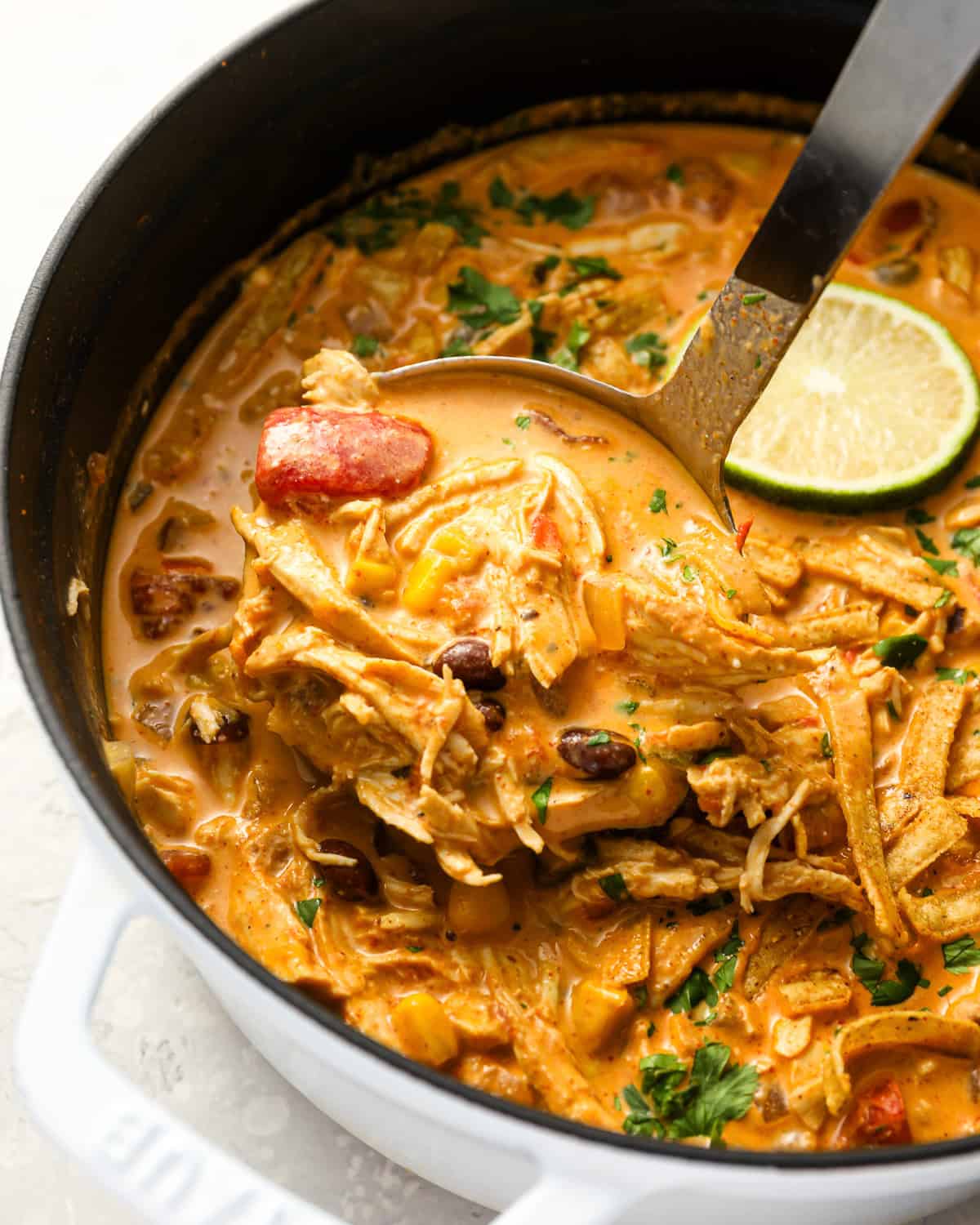 scooping chicken enchilada soup from a dutch oven with a ladle. 