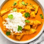 overhead view of a serving of chicken curry in a bowl with rice and cilantro.