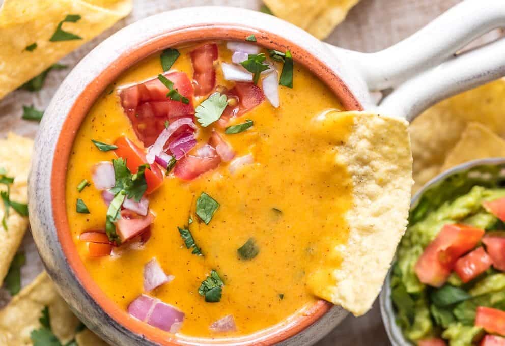 a chip submerged into queso dip
